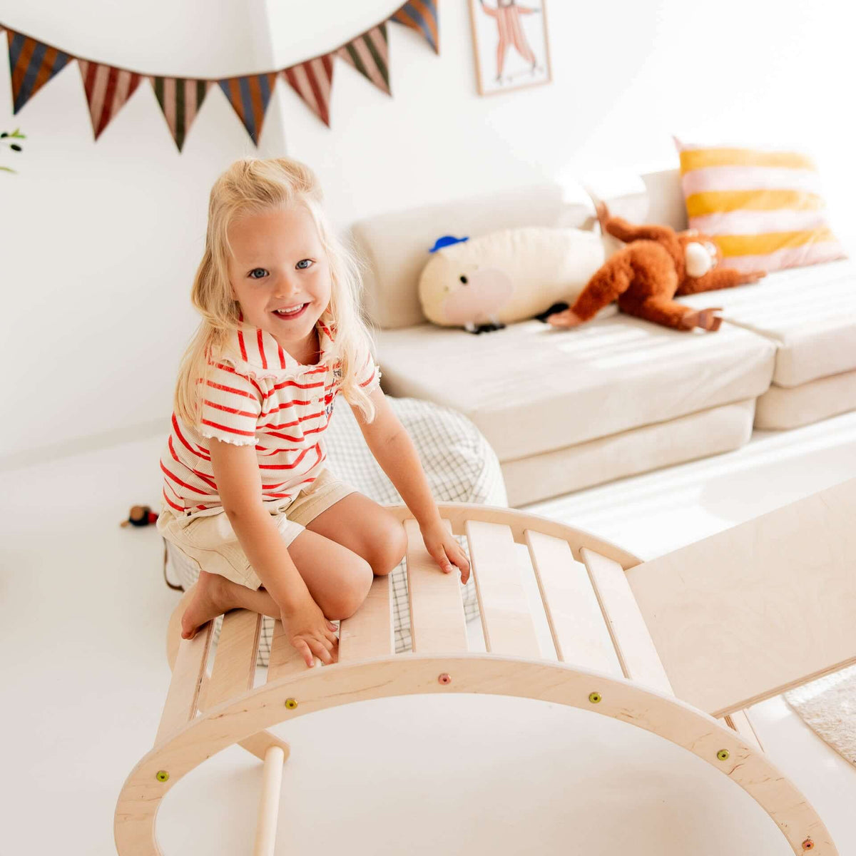 Fröhliches Mädchen auf dem Kletterdreieck Äffchen, das aus Holz gefertigt ist, spielt in einem hellen Kinderzimmer.