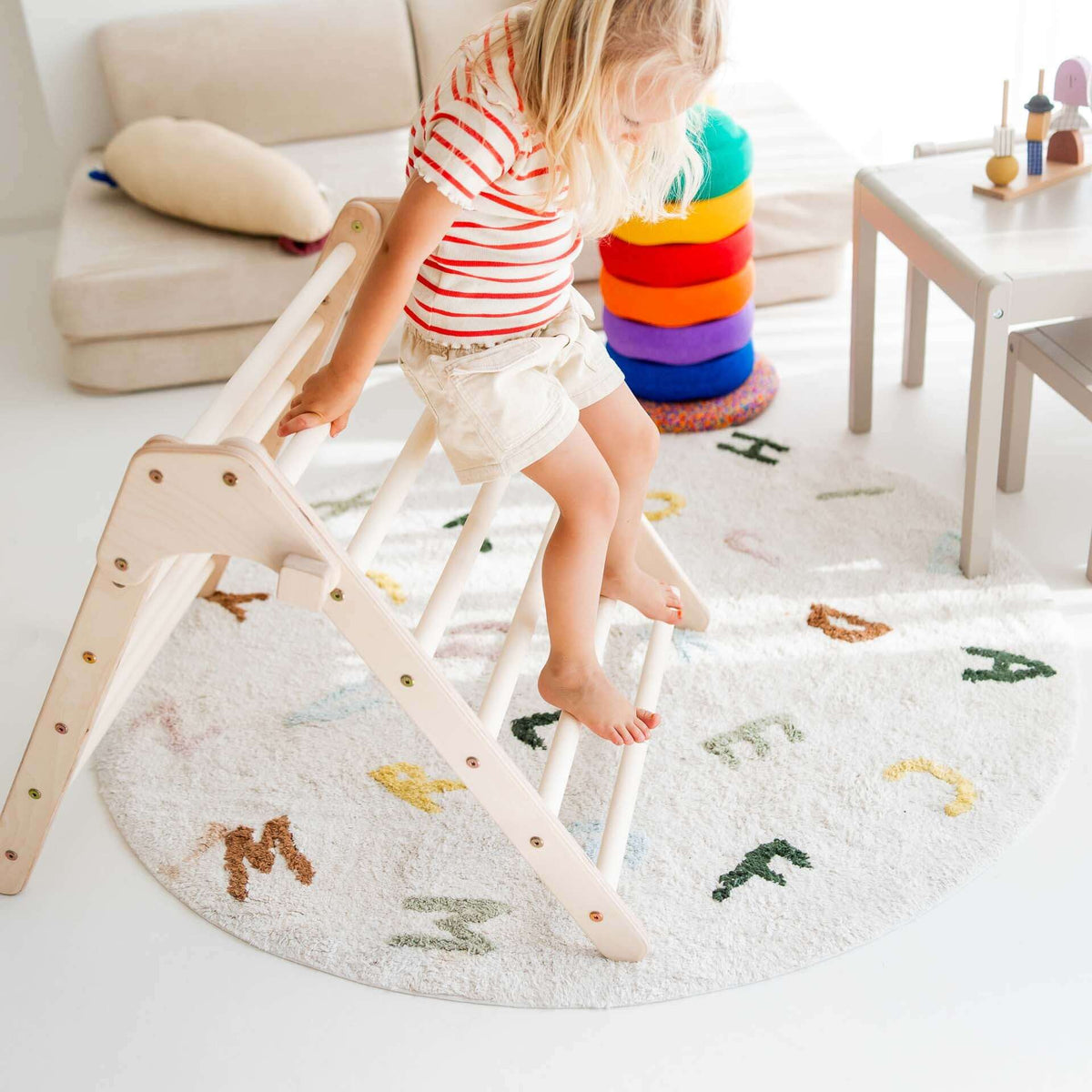 Kind klettert am faltbaren Kletterdreieck Lina auf einem bunten Teppich im Kinderzimmer