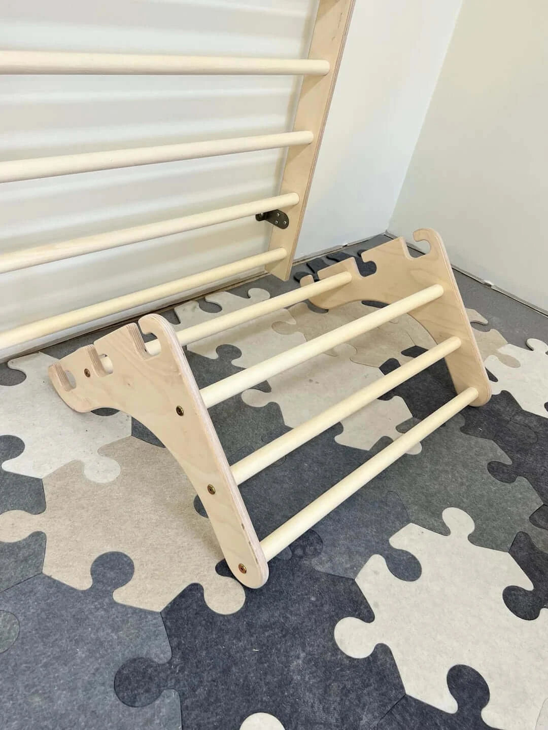 Kletterwand für Kinder aus Holz mit abnehmbarem Klimmzugteil auf einem bunten Puzzle-Bodenbelag.