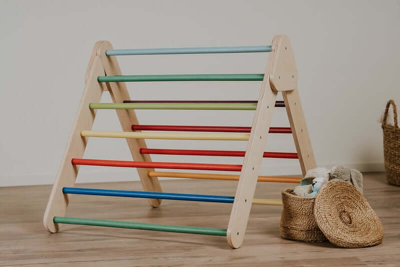 Kind zieht sich am Pikler Kletterdreieck hoch und kommt ins Stehen