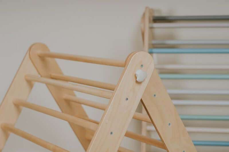 Baby spielt am Pikler Kletterdreieck und zieht sich an den Holzstangen hoch