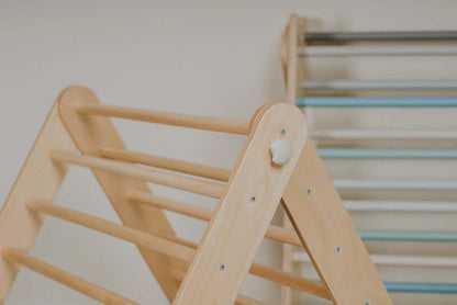 Baby spielt am Pikler Kletterdreieck und zieht sich an den Holzstangen hoch